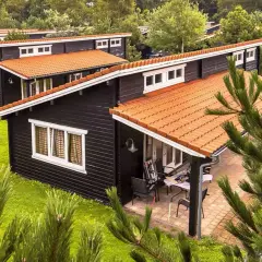 Czarny bungalow z pomarańczowym dachem, otoczony zielenią. Na werandzie stolik i krzesła.
