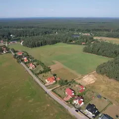 Widok z lotu ptaka na wieś otoczoną lasem. Działka budowlana o powierzchni 1 ara to niewielki kwadrat, idealny na mały domek.
