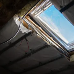 Widok od spodu na okienko w dachu, widać instalację elektryczną i izolację.