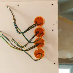 Instalacja elektryczna w trakcie budowy. Widoczne puszki instalacyjne i kolorowe przewody wychodzące ze ścianki działowej z karton-gipsu.