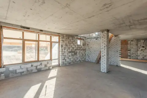 Wnętrze w budowie z betonowym stropem filigran. Ściany z bloczków i cegieł, duże okna, betonowa podłoga.