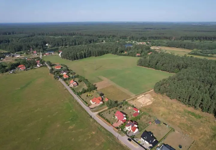 Widok z lotu ptaka na wieś otoczoną lasem. Działka budowlana o powierzchni 1 ara to niewielki kwadrat, idealny na mały domek.