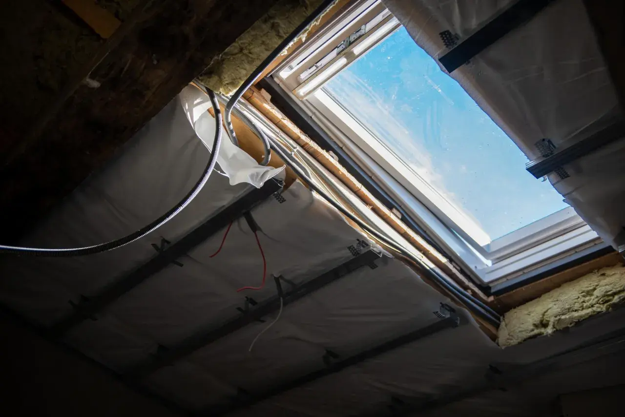 Widok od spodu na okienko w dachu, widać instalację elektryczną i izolację.
