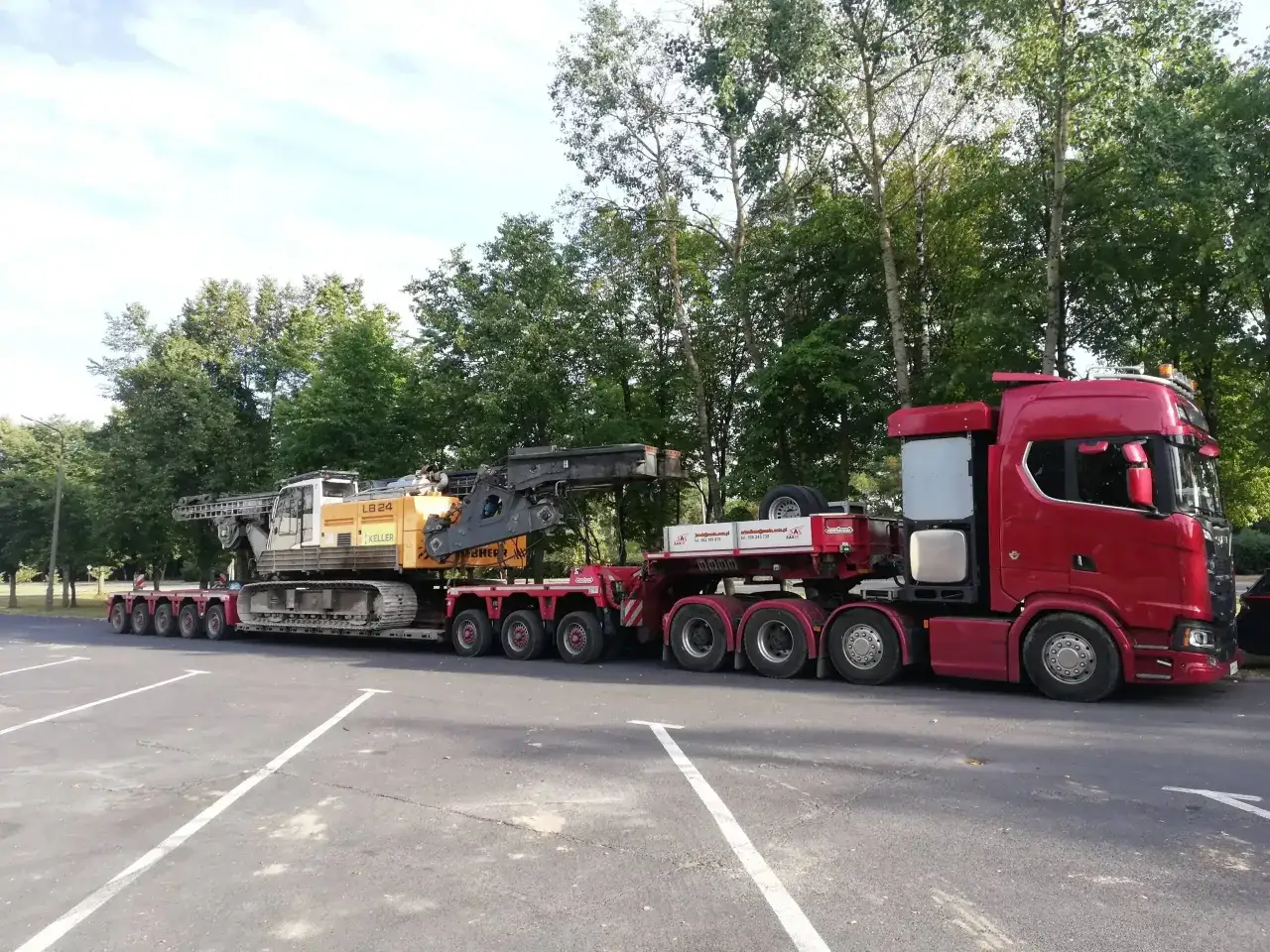 Czerwony ciągnik siodłowy z naczepą transportuje koparkę. Ogromne gabaryty maszyny budowlanej wymagają specjalistycznego transportu.