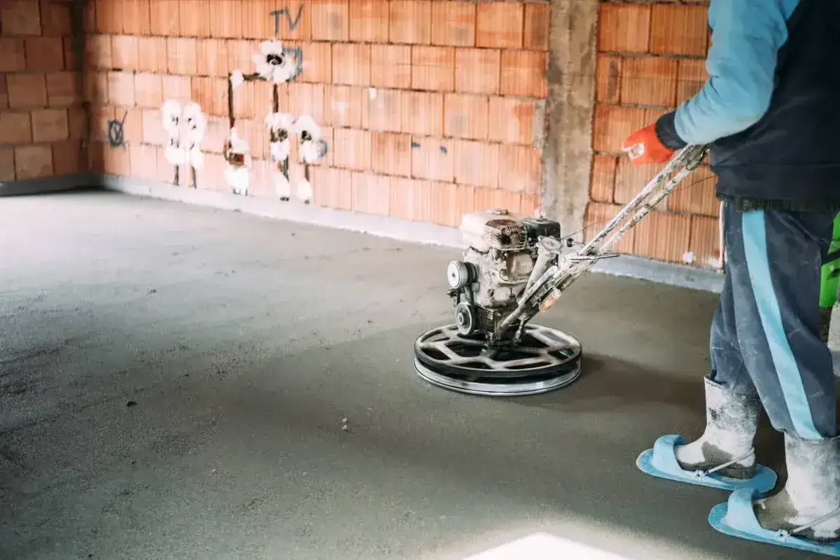 Pracownik wygładza świeży beton za pomocą mechanicznej zacieraczki. Czas, ile schnie beton, zależy od wielu czynników.