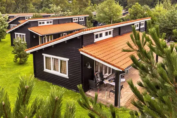 Czarny bungalow z pomarańczowym dachem, otoczony zielenią. Na werandzie stolik i krzesła.